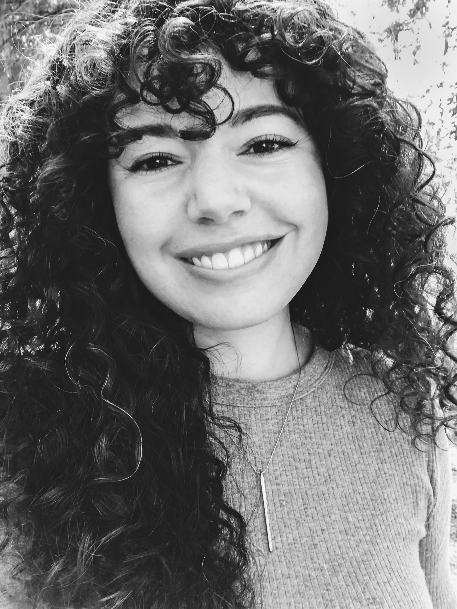 Black and white portrait photo of the artist who has dark curly hair and is smiling warmly.