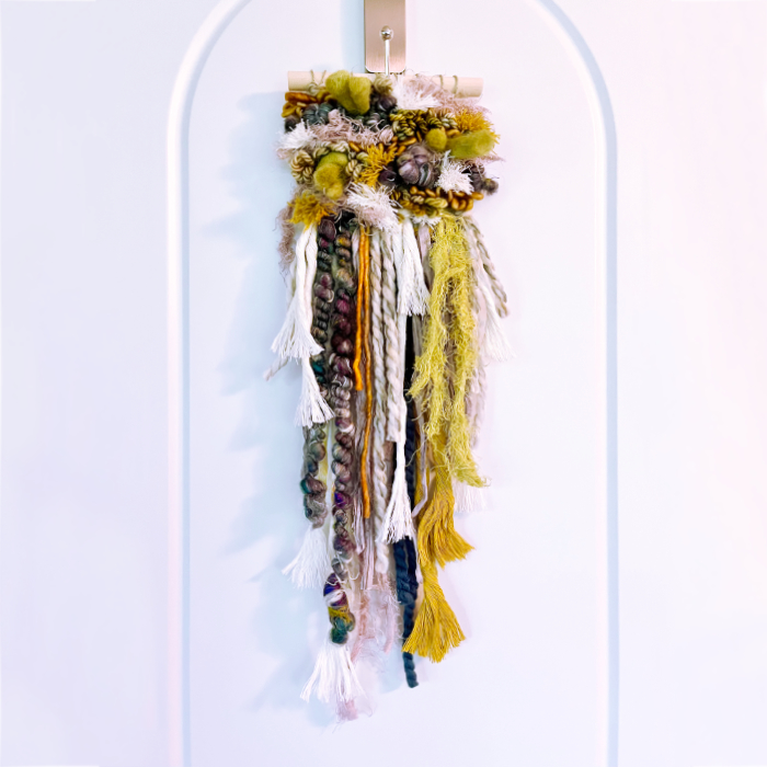 Abstract woven wall hanging dripping with layers of vibrant colors and textures inspired by nature.